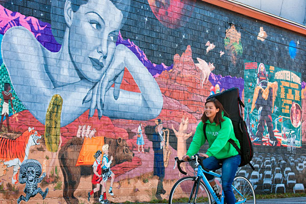 Student riding bike in front of wall mural